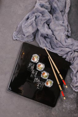 Sushi Set nigiri ve suşi rulo olarak soya sosu, demir demlik ve çubuk siyah taş doku arka plan üzerinde koyu seramik tabak. Üstten Görünüm alanına sahip. Japonya menü. Kare görüntü
