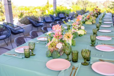 Taze çiçekler ve zarif masa eşyalarıyla süslenmiş, Manzaralı Manzarada Büyüleyici Bir Toplanma İçin Hazır Bir Açık Yemek Masası.