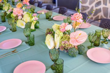 Zarif Yemek Kurulumu Renkli Çiçek Düzenlemeleri ve Şık Bardaklarda Taze Sebzeler ve Yumuşak Yeşil Masa örtüsünde Akşam Yemeği