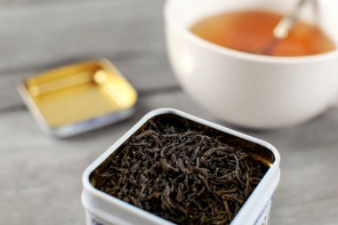 Bulanık fincan sıcak amber ile metal teneke içinde gevşek çay siyah iç arka planda.
