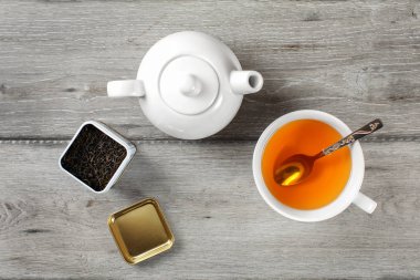 Tablo üstten görünüm - pirinç çay caddy, beyaz porselen çaydanlık ve gümüş kaşık ve sıcak kehribar içecek, seramik kupa gri ahşap masa.