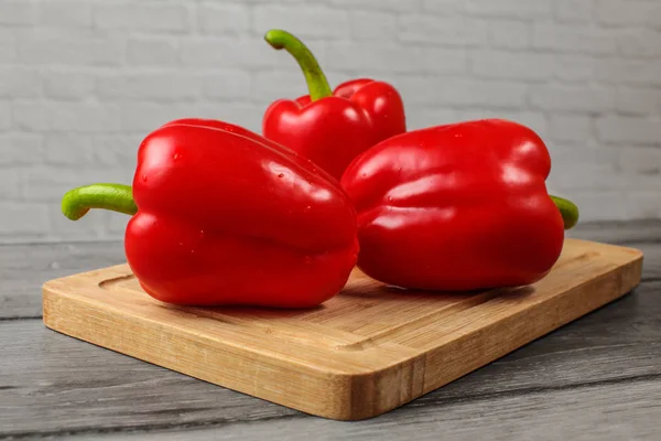 Drei Leuchtend Rote Paprika Auf Altem Holzschneidebrett — Stockfoto