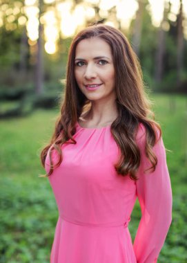 Bahar Park güzel altın günbatımı ışığı ile fotoğraflandı pembe elbise genç kadın uzun siyah saçlı.