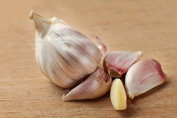 Garlic bulb, some of cloves separated, and one peeled, on old cutting board with many scratches.