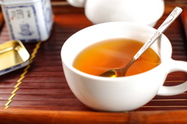 Beyaz porselen fincan, kaşıkla, dumanı tüten çay bambu tepsi yerleştirilmiş.