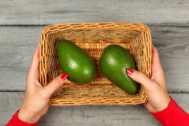 Tablo üstten görünüm - eller genç kadın, kırmızı giyim ve çivi ile iki avokado, kare sepet tutunarak, ahşap Resepsiyon gri.