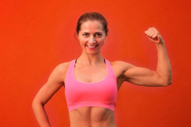 Kırmızı duvarın önünde poz, onun pazı gösteren ve gülümseyen genç atletik kadın.