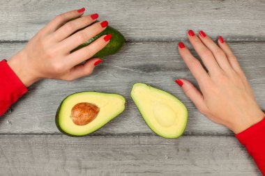 Tablo üstten görünüm - kadın el ve gri ahşap masa üzerinde yarım avokado kesim.