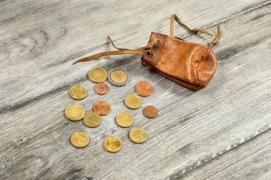 Gri ahşap masanın üstüne dökülen euro para ile eski yıpranmış kahverengi deri bozuk para çantası.