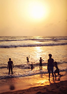 Kalutara, Sri Lanka - 15 Nisan 2017: Silhouettes insan, çoğunlukla ıslak plaj, deniz ve altın günbatımı öğleden sonra ışık arkada oynayan çocuklar.