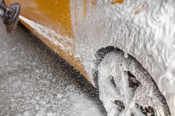 白色洗发水泡沫喷在汽车后轮和侧面 当洗涤洗车场 — 图库照片