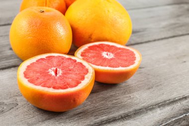 Pembe kırmızı greyfurt rustik masa üzerinde arka planda daha fazla narenciye ile ikiye böldüm.
