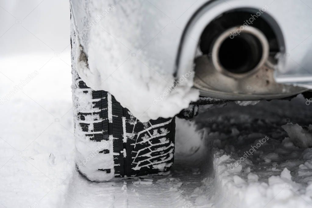 Detail of car tire and exhaust on winter snow
