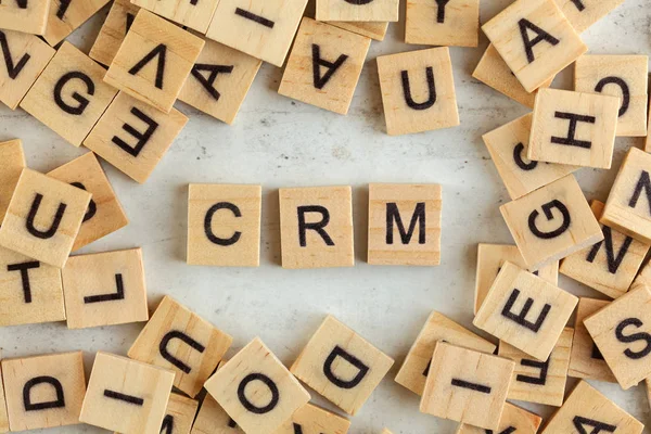 Top down view, pile of square wooden blocks with letters CRM stands for Customer Relationship Management on white board.