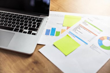 Bütçe sütunu ve daire grafiklere sahip ofis masası, dizüstü bilgisayar ve kağıtlar. 