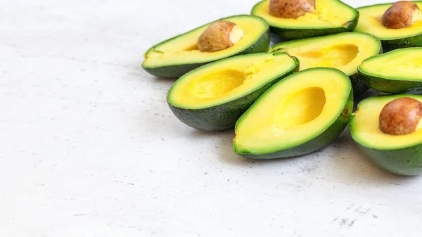 Halved avocados fruits with green yellow pulp, some brown seeds visible on white working board - empty space for text left side — Stock Photo, Image