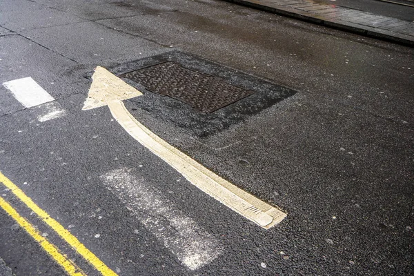Doble línea amarilla y flecha apuntando ligeramente a la derecha sobre asfalto húmedo —  Fotos de Stock