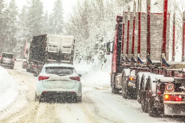 Traffic jam, cars and trucks moving slowly at winter forest road mountain pass during heavy snow blizzard all logos brands on vehicles removed — Stock Photo, Image