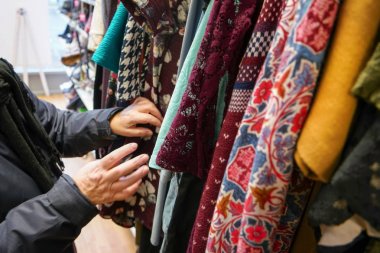 Kıdemli kadın ikinci el tutumlu hayır dükkanı, onu hareket eden elleri üzerinde detay giysi geçiyor.