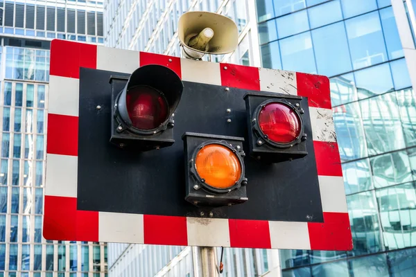 Board with red and white squares, orange traffic lights and speaker, used for signal during roadworks, blurred modern office buildings in background