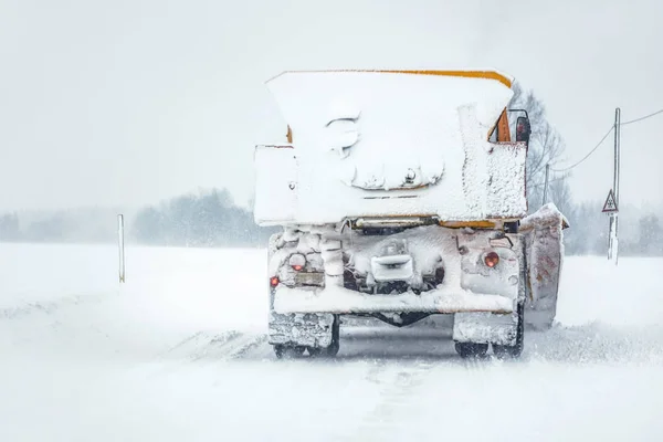 Plow gritter truck on snow covered road during snowstorm, view from car behind — Stock Photo, Image