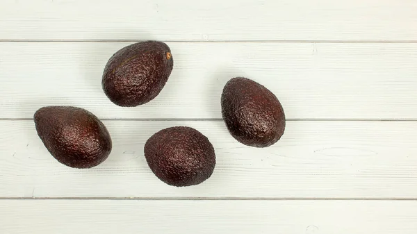 Four ripe brown avocados on white boards desk. Tabletop view.