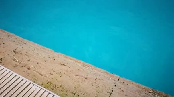 Lado de una piscina, borde de piedra travertino, bañado por pequeñas olas de agua turquesa iluminadas por el sol . — Vídeos de Stock