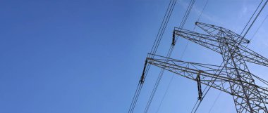 Mavi gökyüzüne karşı yüksek voltaj kablolarıyla çelik elektrik pilonu yapımına bakıyorum. Elektrik enerji endüstrisi için geniş pankart ve sol tarafta metin için boşluk