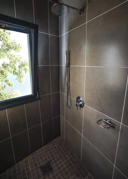 Μοντέρνο μπάνιο στο δωμάτιο του ξενοδοχείου, ντους χάλυβα, δίπλα στο παράθυρο με πράσινα φύλλα στο δέντρο πίσω — Φωτογραφία Αρχείου