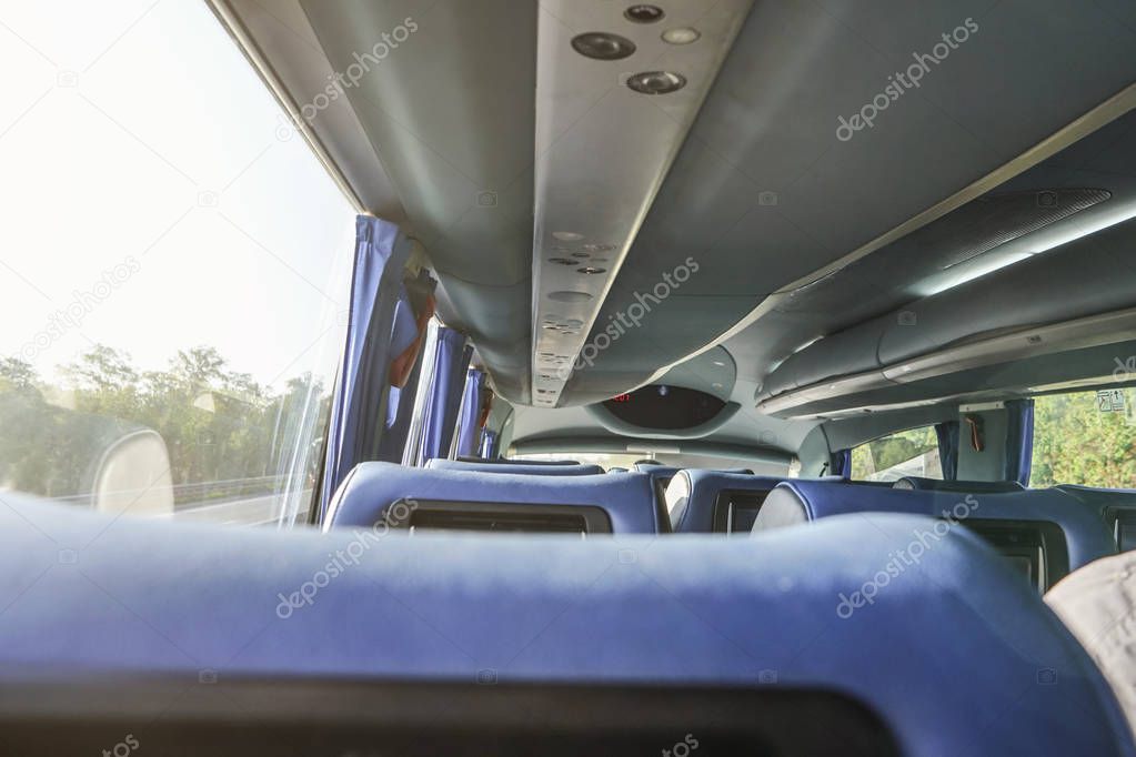 Row of empty blue seats in coach bus, sunny day behind window, view from behind