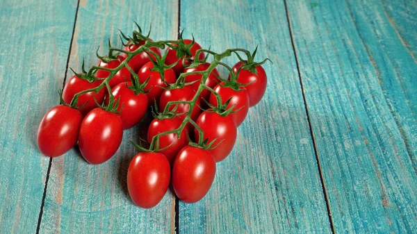 Skupina čerstvých červených rajčat se zelenými kmenovou révou na dřevěných tabulách vybarvených modře, místo pro text na pravé straně — Stock fotografie