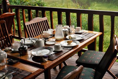 Sabah kahvaltıdan sonra ahşap masa - tabak ve kahve fincanları, kül tablası nda popo, yarım boş süt sürahi, arka planda bulanık yeşil yeşillik kalır - tropikal tatil beldesi