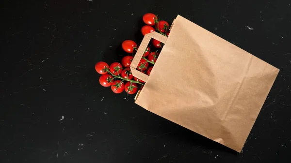 Top down view, brown paper shopping bag with cherry tomatoes laying on black marble like desk, space for text left down corner — Stock Photo, Image