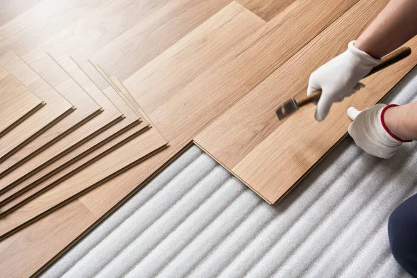 Instalación de piso laminado, detalle en las manos del hombre sosteniendo martillo en guantes textiles, sobre la capa base de espuma blanca — Foto de Stock