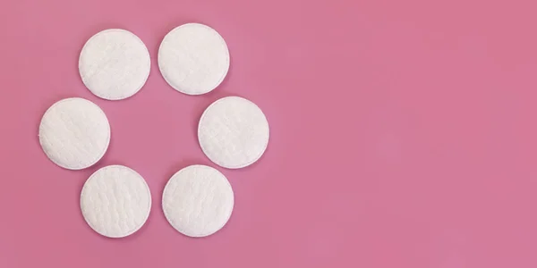 Vue du haut vers le bas, 6 tampons de coton de nettoyage du visage disposés en cercle, sur une planche rose, large espace de bannière pour le texte à droite — Photo