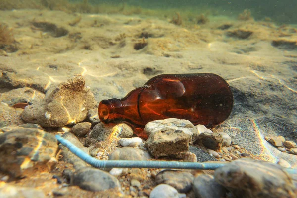 Pequena garrafa de cerveja marrom e palha de plástico azul em bott mar arenoso — Fotografia de Stock