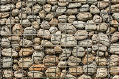 Yuvarlak kayaçlardan yapılmış duvar, çelik tel ağ ile sabitlenmiş (demir taş