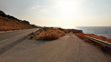 Öğleden sonra güneş ilerlüne kadar uzanan asfalt yolda parlar, mesafe deniz - Kuzey Kıbrıs'ın Karpas bölgesinde tipik manzara