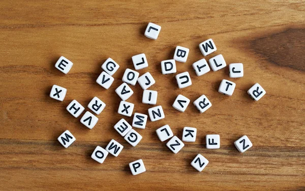 Kleine witte kubus kralen met verschillende letters verspreid op houten bord, uitzicht vanaf boven — Stockfoto