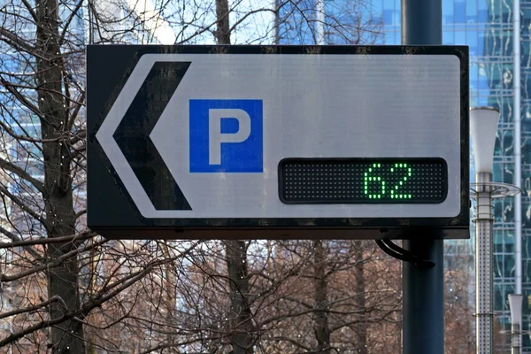 Tablero de señales de tráfico que muestra el número de plazas de aparcamiento y la flecha que apunta al estacionamiento, el texto se puede agregar al espacio en blanco, árboles borrosos y edificios de fondo — Foto de Stock