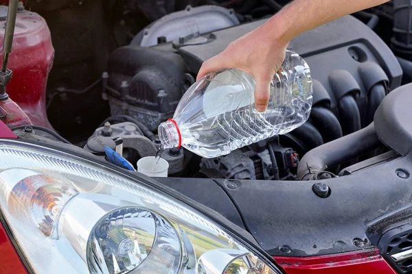 Uomo versando acqua distillata alternativa ecologica al lavaggio del fluido al serbatoio della lavatrice in auto, dettaglio a portata di mano tenuta bottiglia di plastica trasparente — Foto Stock