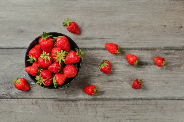 Vista de la mesa, pequeño cuenco de cerámica negra con fresas, algunos — Foto de Stock