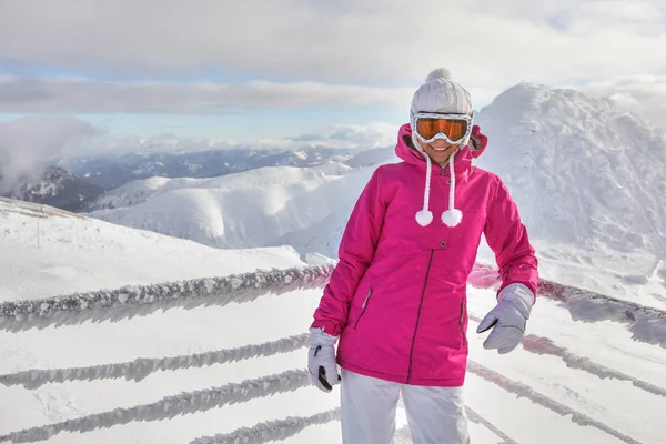 Молодая женщина в розовой куртке, в лыжных очках, опирающаяся на снег — стоковое фото