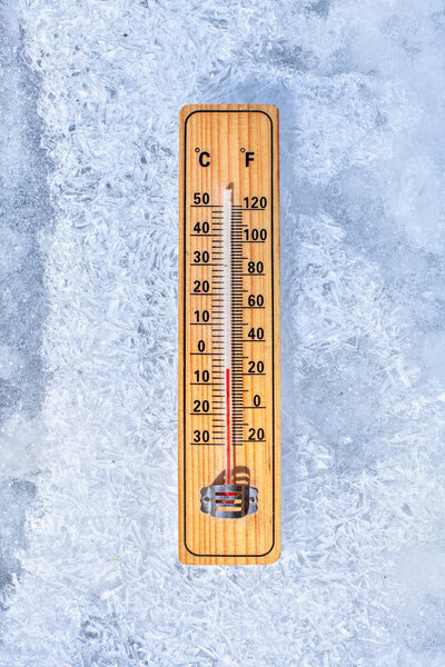 Thermometer laying on ice, showing minus 5 degrees. Sun shining 