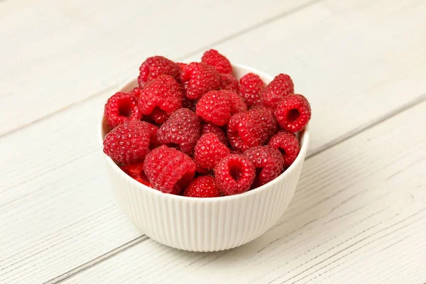 Small porcelain cup with raspberries on white boards desk. — Stock Photo, Image