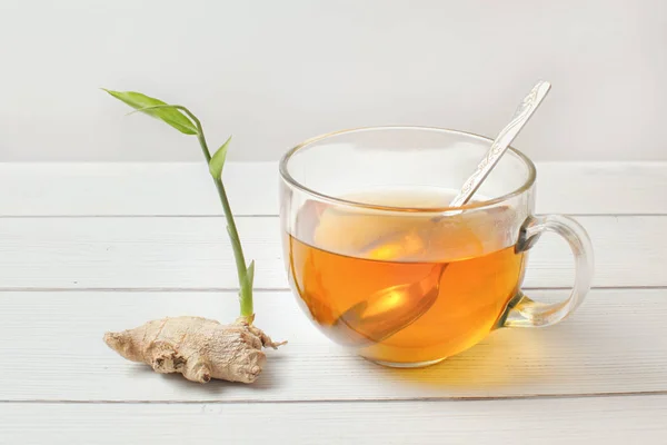 Spoon in glass cup of hot amber tea, dry ginger root with green — Stock Photo, Image