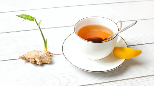 Porcelain cup with hot amber tea, and slice of lemon, dry ginger — Stock Photo, Image