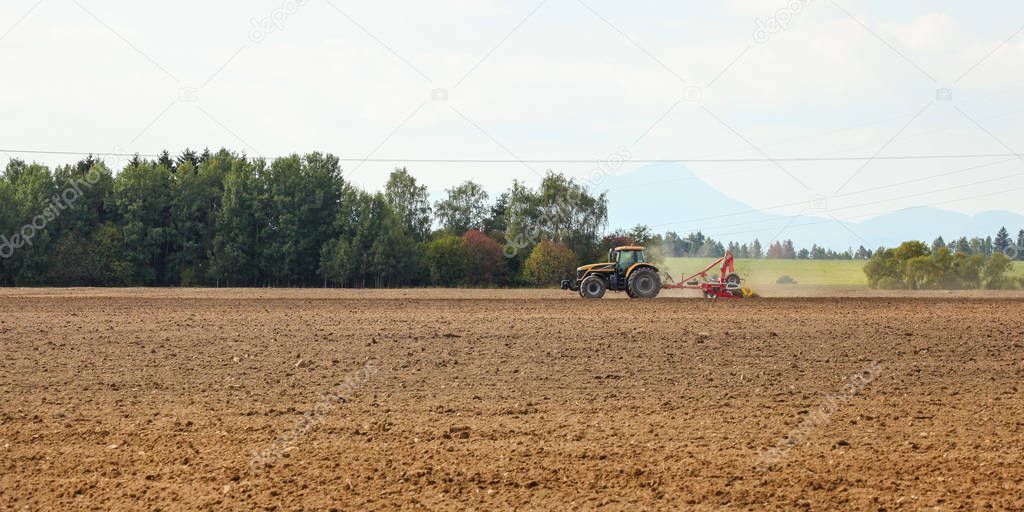 Tractor sowing in empty field on countryside with some mountains