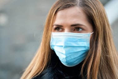Tek kullanımlık mavi virüs kullanan genç bir kadın ağız maskesi takıyor, yakın plan bir portre. Coronavirus covid-19 salgın önleme kavramı