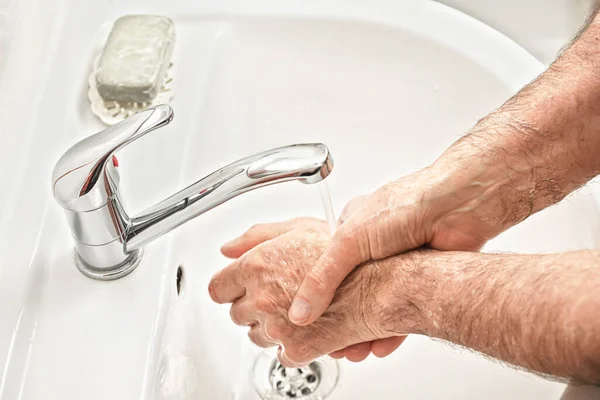 Senior elderly man his hands and wrist with soap under tap water faucet, detail photo. Can be used as hygiene illustration concept during coronavirus / covid-19 outbreak prevention